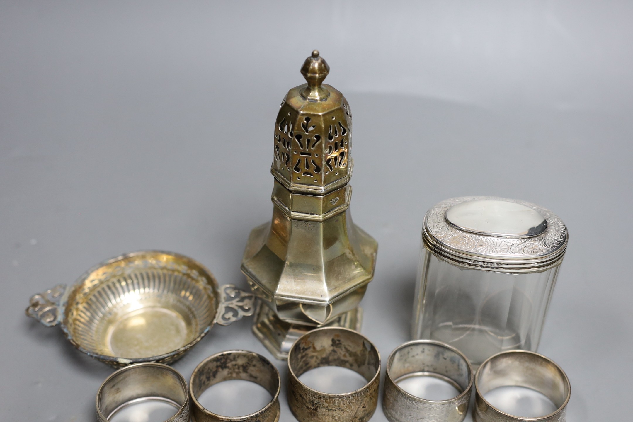 A George V silver sugar caster, London, 1933, 17cm, a silver topped glass toilet jar, a silver bon bon dish and five silver serviette rings.